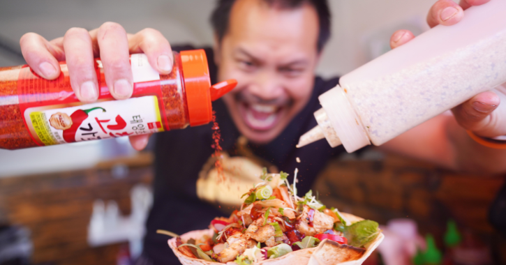 man pouring chilli flakes and sauce onto a wrap at Bishop Auckland Food Festival